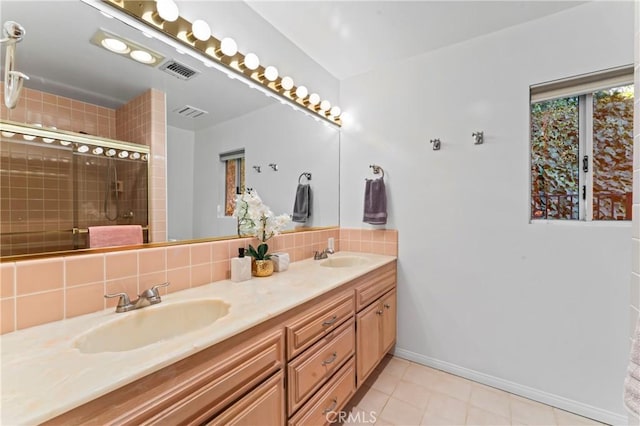 bathroom with a shower with door, vanity, tile patterned flooring, and backsplash