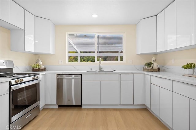 kitchen with appliances with stainless steel finishes, sink, light hardwood / wood-style flooring, and white cabinets