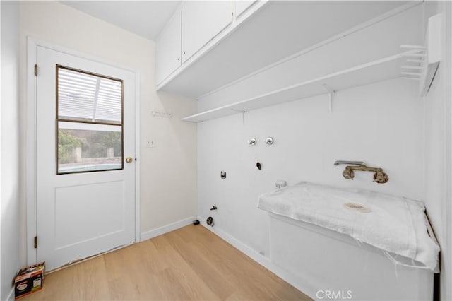 clothes washing area featuring gas dryer hookup, cabinets, and light wood-type flooring