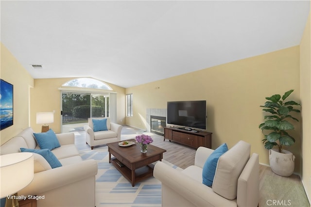 living room featuring a tiled fireplace, lofted ceiling, and light wood-type flooring