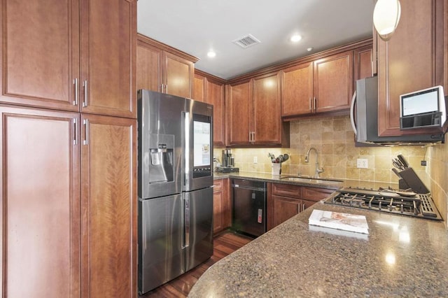 kitchen with sink, stainless steel appliances, dark hardwood / wood-style flooring, decorative backsplash, and dark stone counters