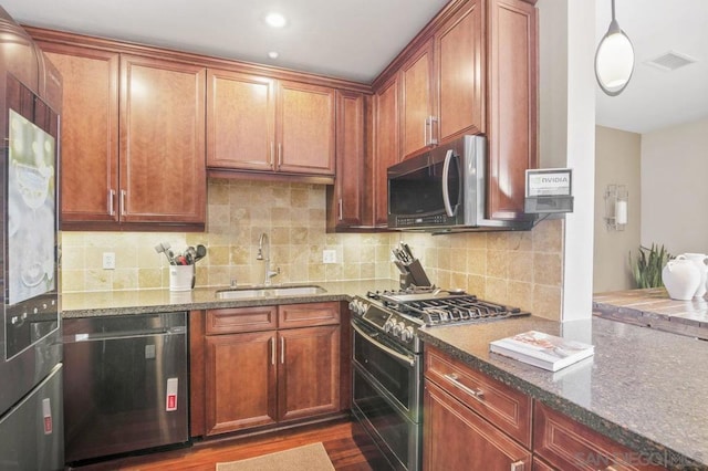 kitchen featuring sink, dark stone countertops, decorative backsplash, hanging light fixtures, and stainless steel appliances