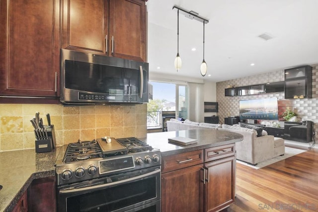 kitchen with backsplash, dark stone counters, hanging light fixtures, light hardwood / wood-style floors, and stainless steel appliances