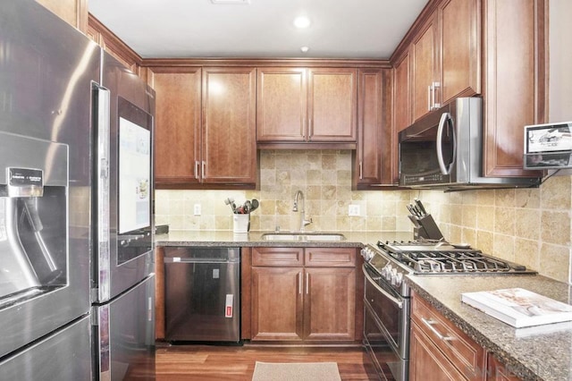 kitchen with appliances with stainless steel finishes, hardwood / wood-style floors, tasteful backsplash, sink, and dark stone countertops