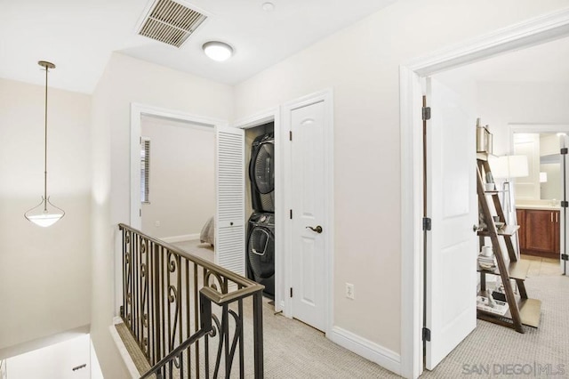 hallway featuring stacked washer and dryer and light colored carpet