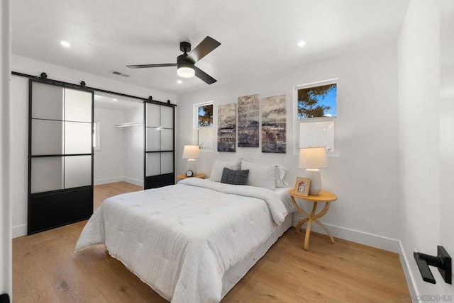 bedroom featuring ceiling fan, a barn door, and light wood-type flooring