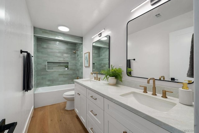 full bathroom with hardwood / wood-style flooring, tiled shower / bath, vanity, and toilet