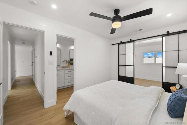 bedroom featuring ceiling fan, ensuite bath, a barn door, and light hardwood / wood-style flooring