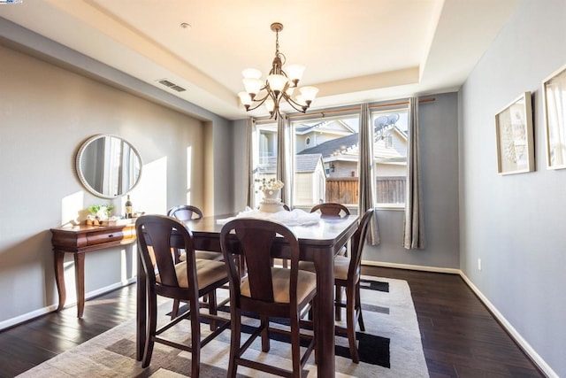 dining area with a raised ceiling, dark hardwood / wood-style floors, and an inviting chandelier