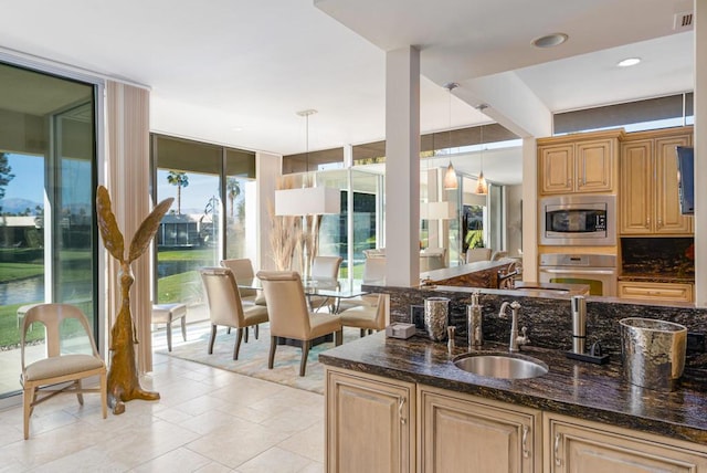 kitchen featuring pendant lighting, sink, a wall of windows, dark stone counters, and stainless steel appliances