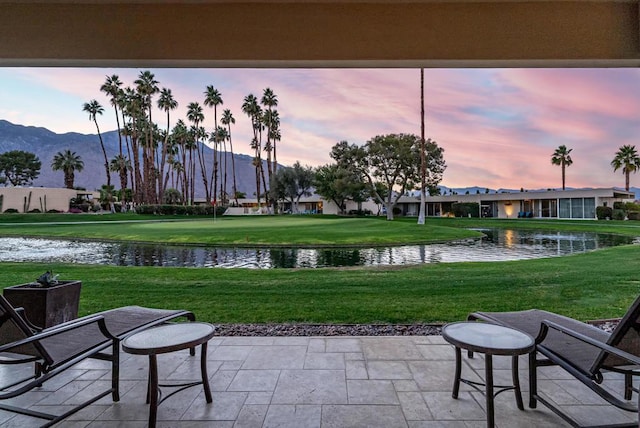 patio terrace at dusk with a water and mountain view and a yard