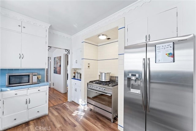 kitchen with white cabinetry, crown molding, dark hardwood / wood-style floors, stainless steel appliances, and decorative backsplash