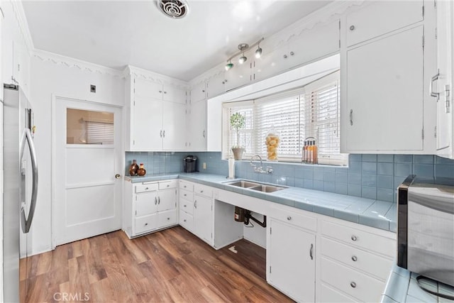 kitchen with white cabinetry, sink, tile counters, and stainless steel refrigerator