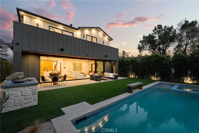 back house at dusk with a fenced in pool, a lawn, an outdoor living space, a patio area, and a balcony