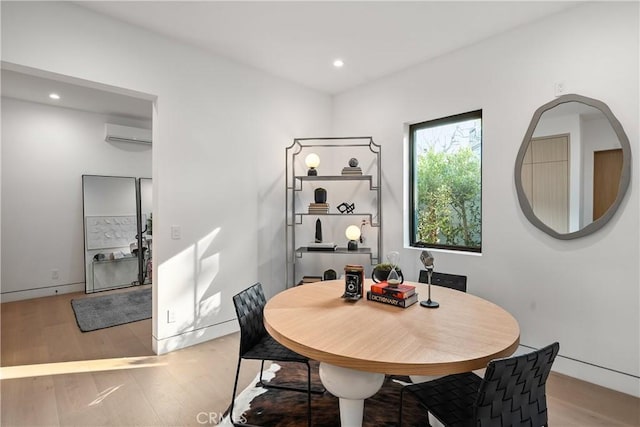 dining area with a wall mounted AC and light wood-type flooring