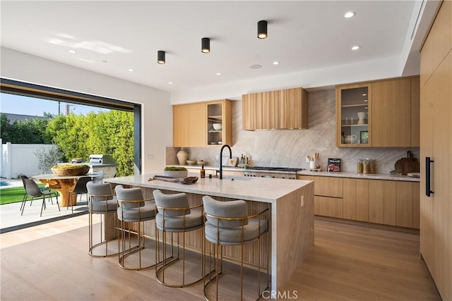 kitchen featuring light brown cabinetry, tasteful backsplash, an island with sink, sink, and light hardwood / wood-style flooring