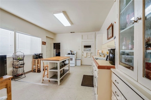 kitchen with sink, tile countertops, white gas stove, and white cabinets