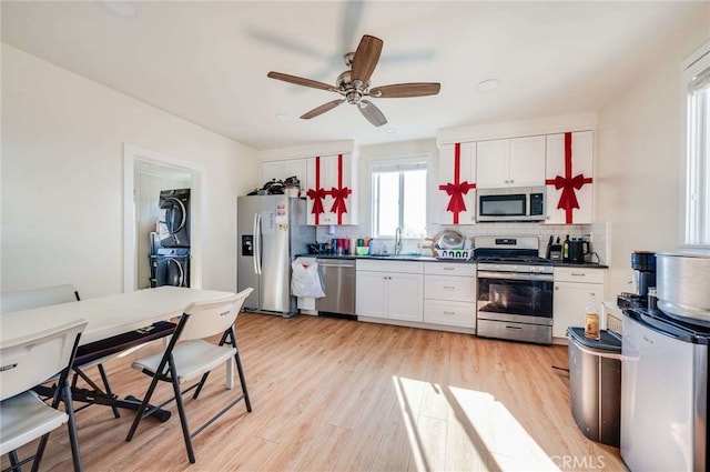 kitchen featuring appliances with stainless steel finishes, stacked washing maching and dryer, sink, and white cabinets