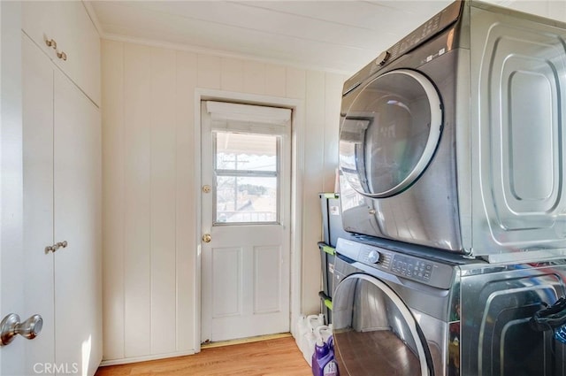 laundry area featuring crown molding, stacked washing maching and dryer, and light wood-type flooring