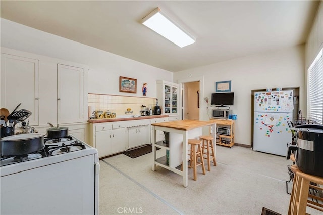 kitchen with a breakfast bar, wood counters, white cabinets, decorative backsplash, and white appliances