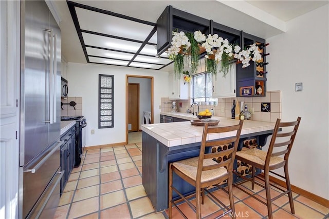 kitchen with a breakfast bar area, white cabinets, backsplash, tile counters, and black appliances