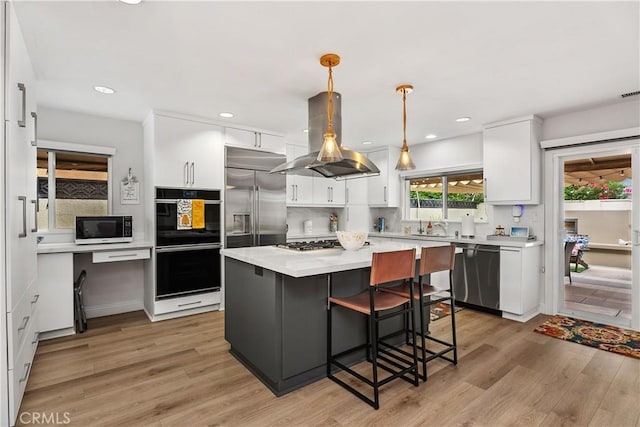 kitchen featuring island range hood, white cabinetry, hanging light fixtures, light hardwood / wood-style floors, and stainless steel appliances