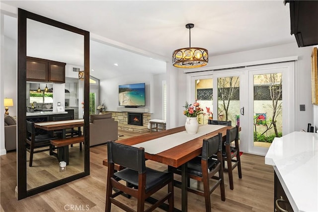 dining area with lofted ceiling, a stone fireplace, and light wood-type flooring