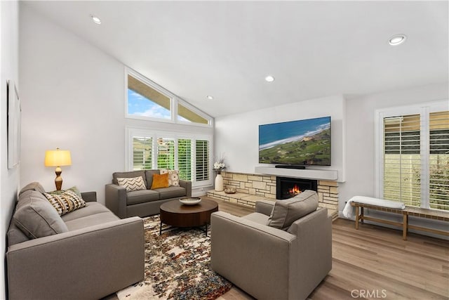 living room featuring a stone fireplace, light hardwood / wood-style flooring, and high vaulted ceiling