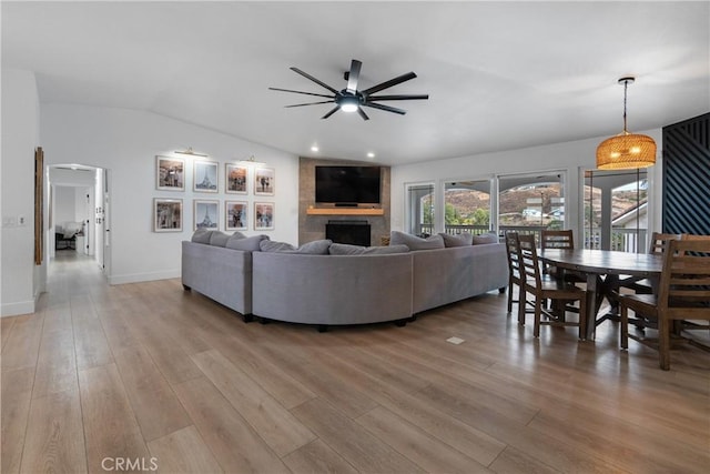 living room featuring ceiling fan, a fireplace, vaulted ceiling, and light hardwood / wood-style flooring