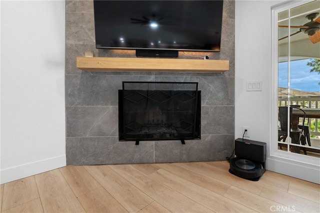 interior details with a tile fireplace, wood-type flooring, and ceiling fan