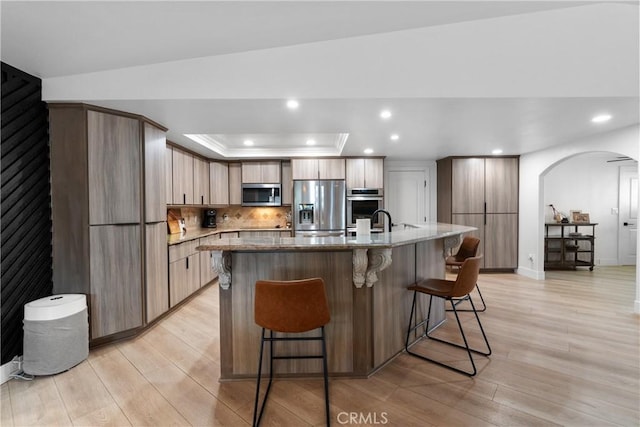 kitchen with light hardwood / wood-style floors, stainless steel appliances, a breakfast bar, and a center island with sink