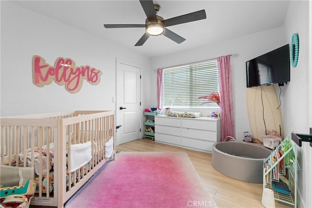 bedroom featuring ceiling fan, a crib, and light wood-type flooring