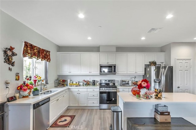 kitchen featuring sink, light hardwood / wood-style flooring, stainless steel appliances, a kitchen breakfast bar, and white cabinets