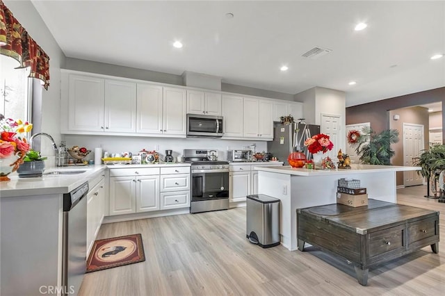 kitchen featuring sink, stainless steel appliances, a center island, light hardwood / wood-style floors, and white cabinets