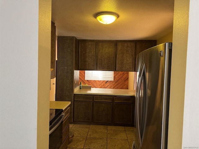 kitchen with stainless steel refrigerator, dark brown cabinetry, electric range oven, and light tile patterned floors