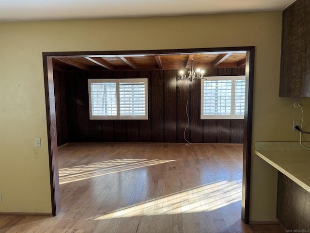 empty room with a healthy amount of sunlight, beam ceiling, and light hardwood / wood-style flooring