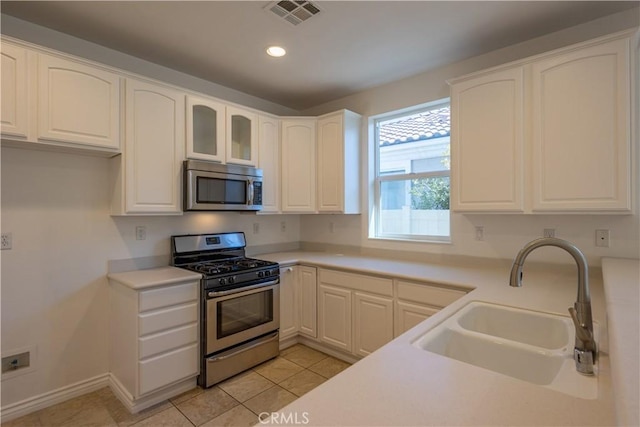 kitchen with light tile patterned floors, appliances with stainless steel finishes, sink, and white cabinets