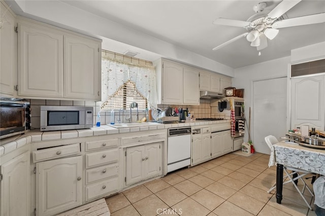 kitchen featuring light tile patterned flooring, tile countertops, dishwasher, sink, and backsplash