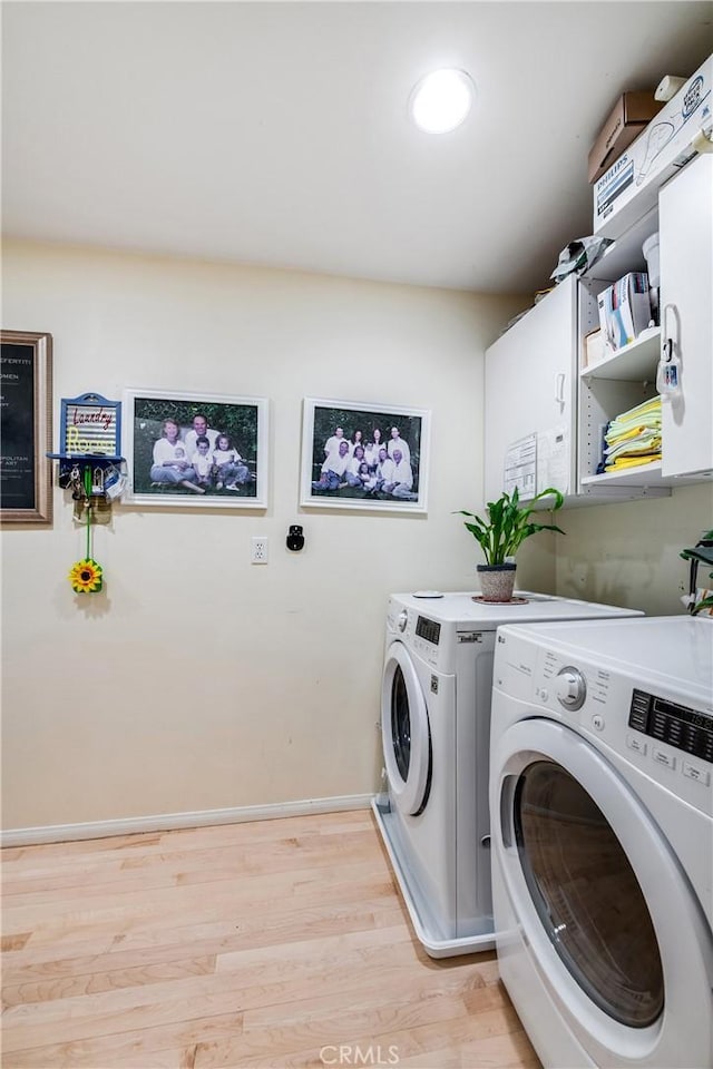 clothes washing area featuring cabinets, separate washer and dryer, and light hardwood / wood-style floors