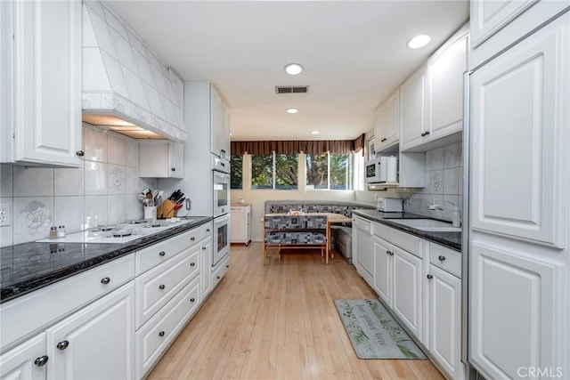 kitchen featuring sink, white cabinets, dark stone counters, white appliances, and light wood-type flooring