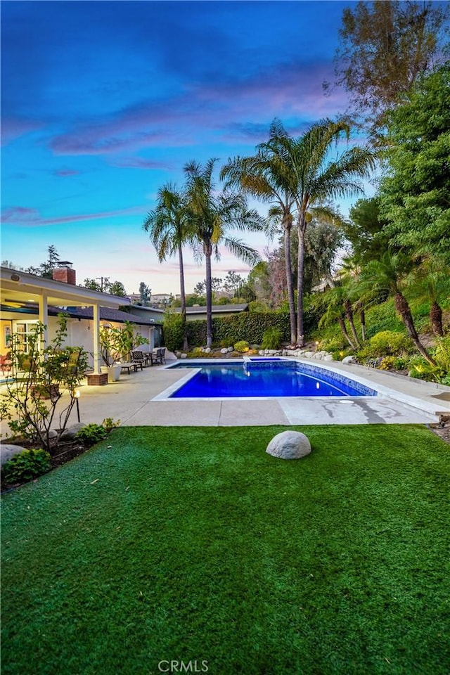 pool at dusk featuring a patio and a yard