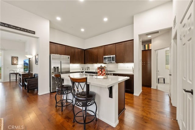 kitchen featuring a kitchen bar, dark brown cabinets, a center island with sink, appliances with stainless steel finishes, and dark hardwood / wood-style floors