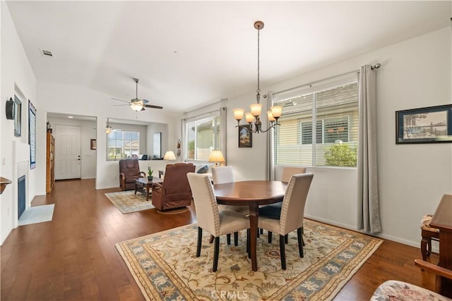 dining space with ceiling fan with notable chandelier, dark hardwood / wood-style floors, and vaulted ceiling