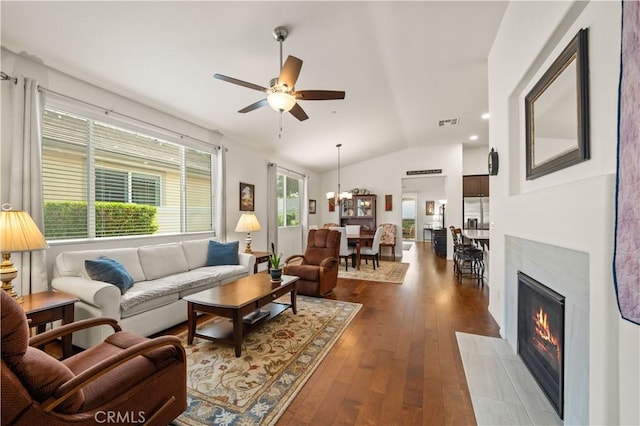 living room with ceiling fan with notable chandelier, dark wood-type flooring, and vaulted ceiling