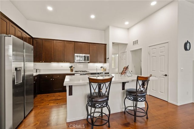 kitchen featuring stainless steel appliances, an island with sink, dark hardwood / wood-style floors, and a kitchen bar