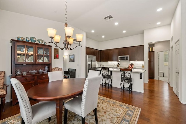 dining area with dark wood-type flooring and an inviting chandelier