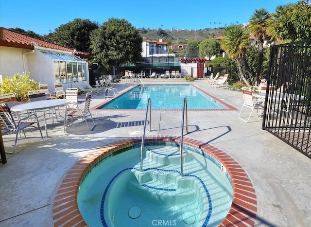 community pool with a patio area, a community hot tub, and fence