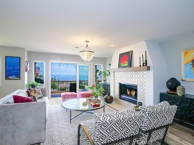 living area featuring a tiled fireplace, visible vents, a notable chandelier, and wood finished floors