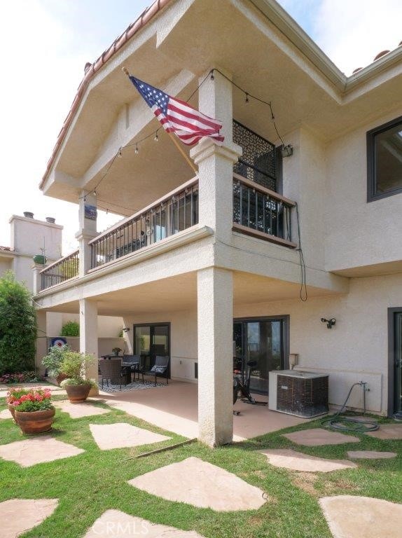 back of house with a balcony, cooling unit, a patio area, and stucco siding