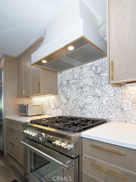 kitchen with exhaust hood, light brown cabinets, dark hardwood / wood-style flooring, high end stainless steel range oven, and backsplash